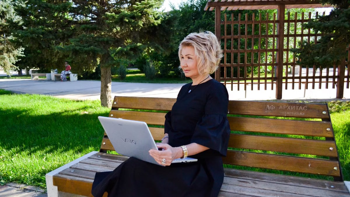 Woman sitting on a bench with a laptop, enjoying a sunny day in a green park setting.